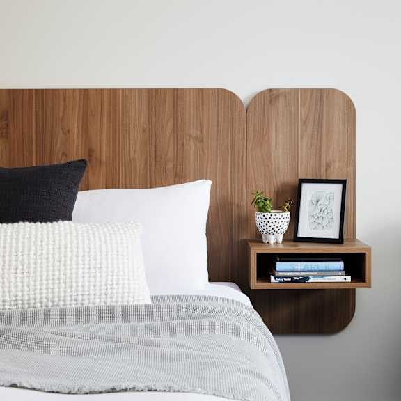 a bed with a wooden headboard and a nightstand with a plant and books