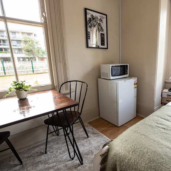 a bedroom with a bed and a desk and a microwave on a refrigerator