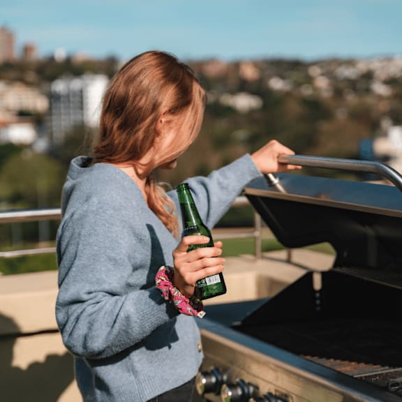 a woman holding a bottle of beer standing next to a grill