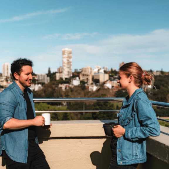 a man and a woman talking on a balcony with a city in the background