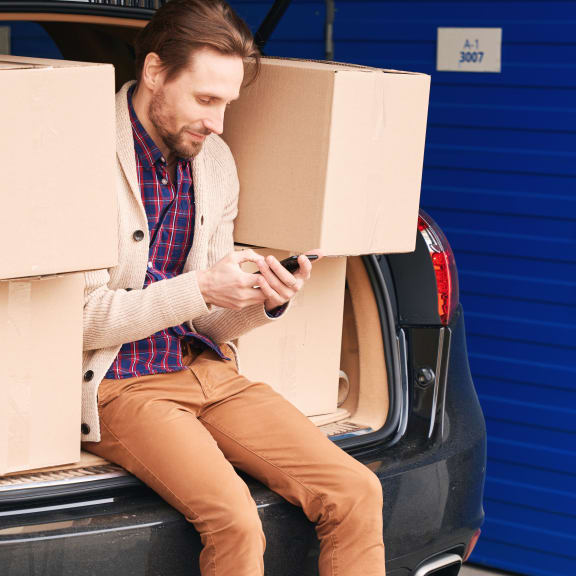a man sitting in the trunk of a car with boxes on his phone