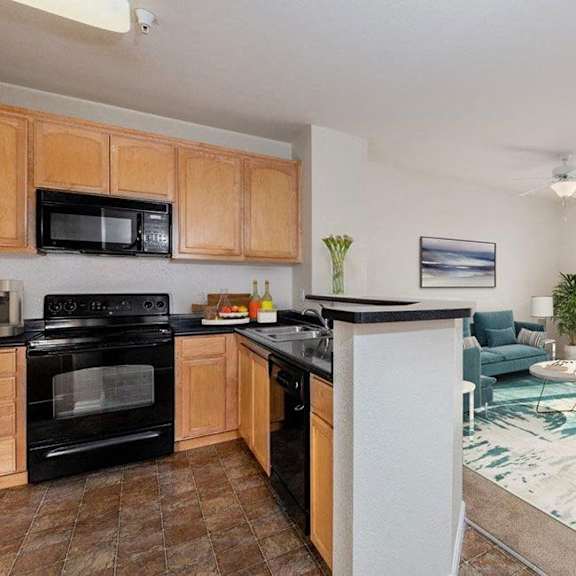 a kitchen with a black oven and microwave, a dining table with chairs, and a living room with a couch and a plant.