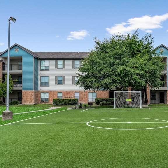 a basketball court is located in the middle of a grassy area in front of apartment buildings.
