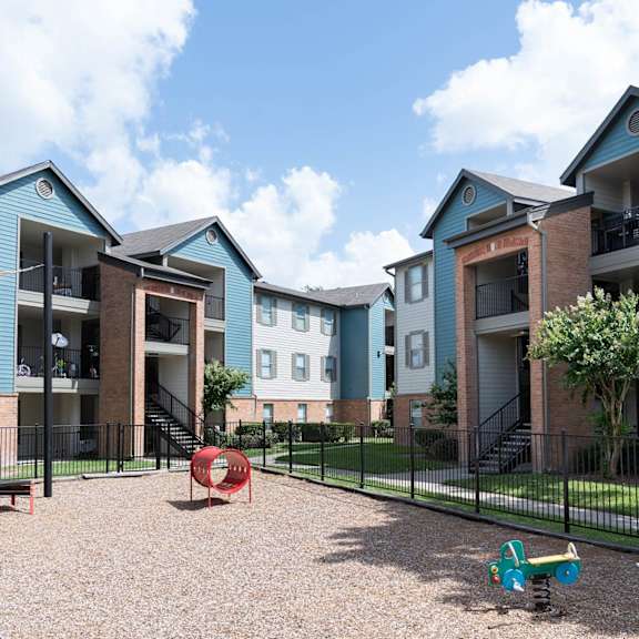 a playground area with a slide and a seesaw in front of apartment buildings.