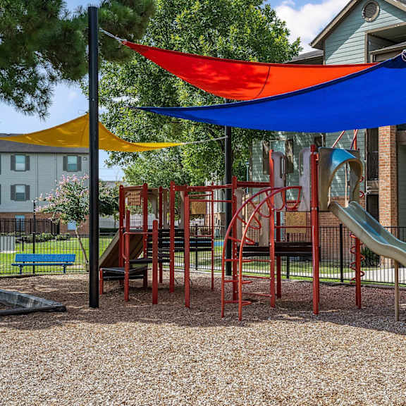 a playground with a red slide and a blue and yellow shade structure.
