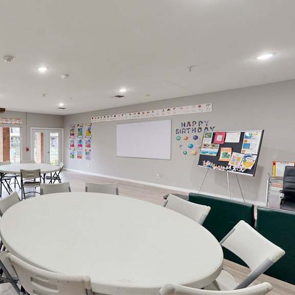 a white table is surrounded by chairs in a room with a whiteboard on the wall.