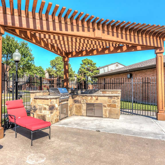 a wooden pergola with red cushioned chairs and a stone fireplace.