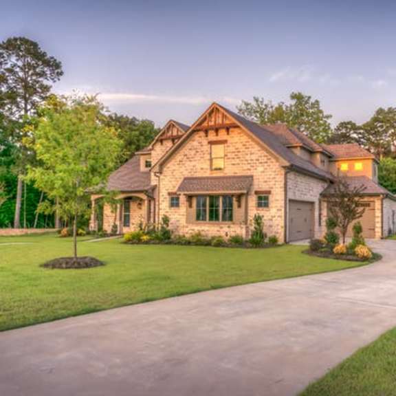 a house with a driveway and a tree in the middle of a grassy area