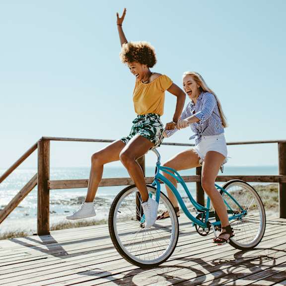 two women riding a bike on a boardwalk on the beach