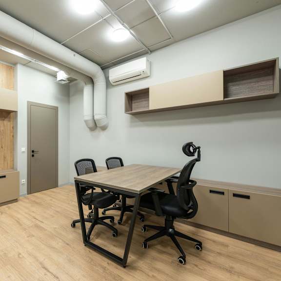 a room with a wooden table and chairs, and a white pipe on the wall.