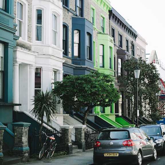 a street with cars parked on the side and a green tree in front of a building.