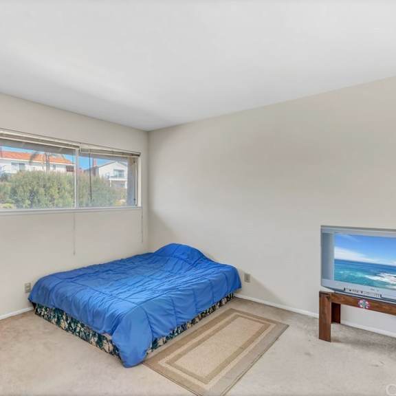 a bedroom with a bed, a television, and a window overlooking the beach.