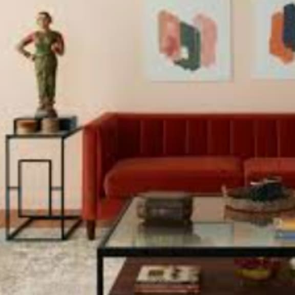 a living room with a red couch, a glass coffee table, and a statue on a small table.