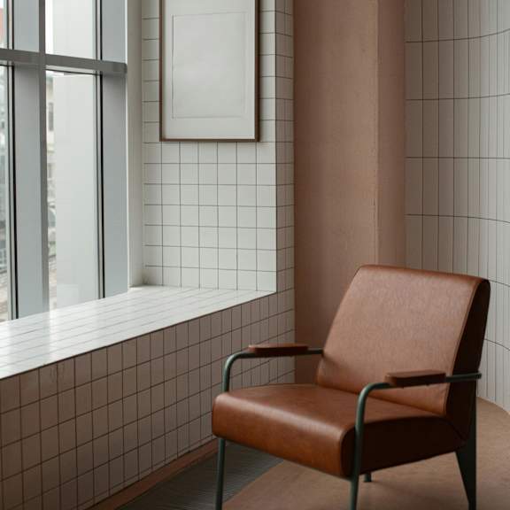 a brown leather chair sits in front of a window with a white frame and a picture on the wall.