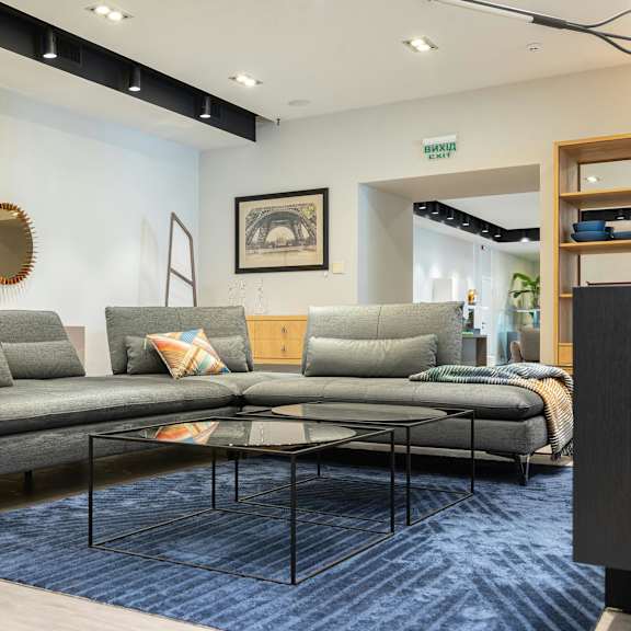 a living room with a grey sofa and a round mirror on the wall.