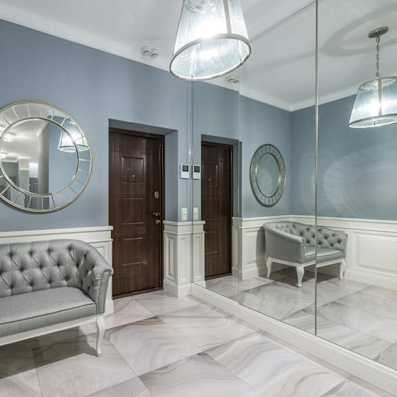 a grey tufted sofa sits in a hallway with a mirrored wall and a round mirror above it.