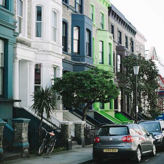 a street with cars parked on the side and a green tree in front of a building.