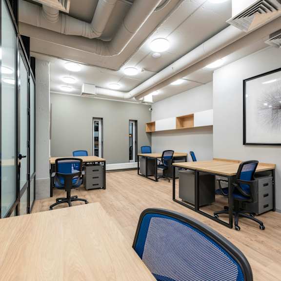 a room with wooden floors and white walls has several desks and chairs.