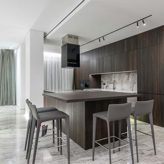 a modern kitchen with a bar area and grey chairs.