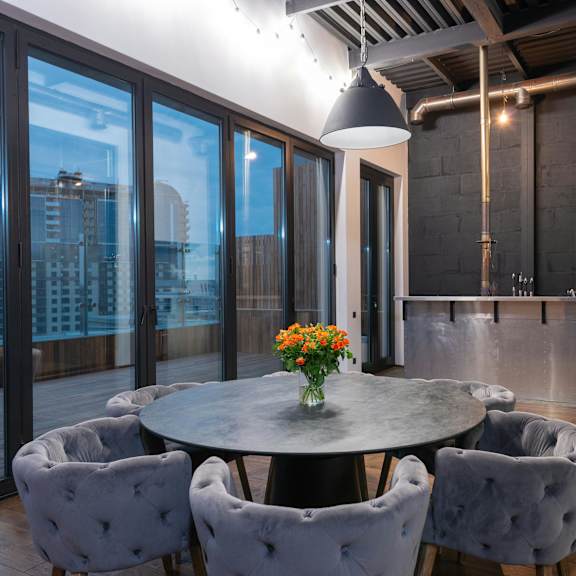 a round table with grey chairs and a vase of flowers in the middle.