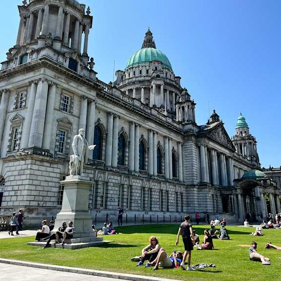 people sitting on the grass in front of a large building