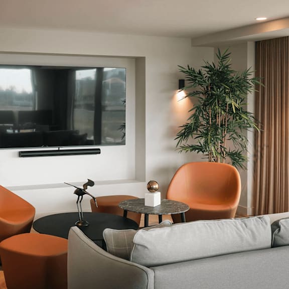a modern living room with a grey sofa, orange chairs, and a flat screen tv mounted on the wall. at cherrywood apartments, d18 vy3v, dublin 18