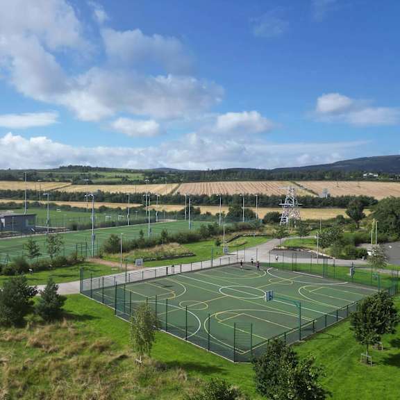 a basketball court surrounded by a green fence with a cloudy blue sky in the background. at cherrywood apartments, d18 vy3v, dublin 18