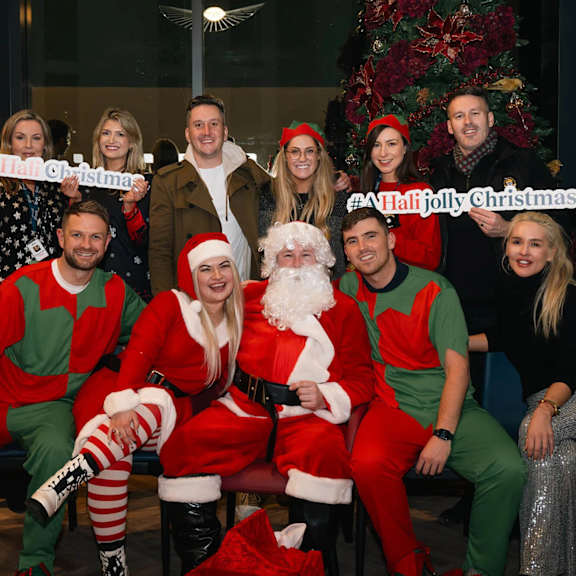 a group of people dressed as santa and elves are posing for a photo in front of a christmas tree. at cherrywood apartments, d18 vy3v
