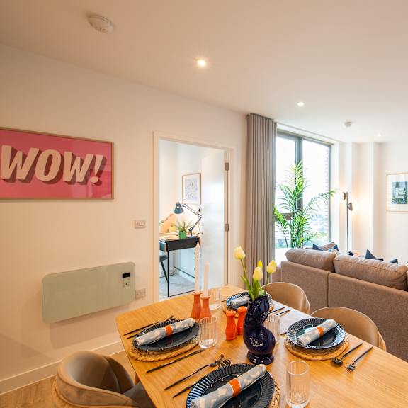 Thumbnail 2 of 8 A dining table set with plates and cutlery is in the foreground of a bright living room.
