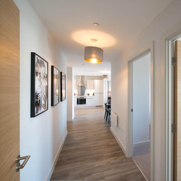 Thumbnail 2 of 6 A hallway with a light on the ceiling and pictures on the wall.