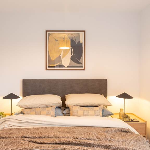 Thumbnail 7 of 11 A bed with a grey headboard and a blanket with a pillow on it.