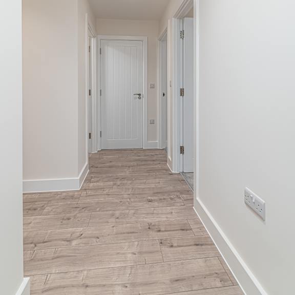 Thumbnail 8 of 12 A long hallway with a white door at the end.