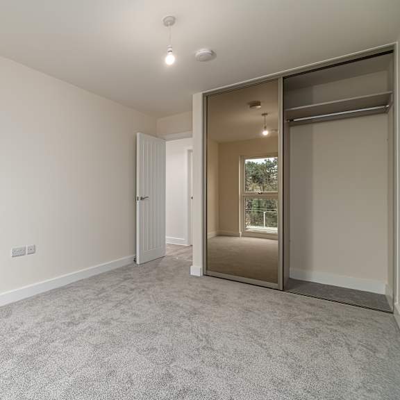 Thumbnail 3 of 12 A room with a grey carpet and a sliding door leading to a balcony.
