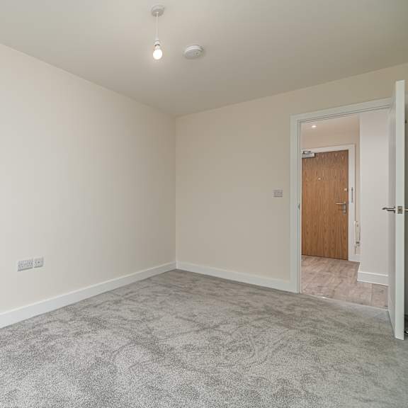 Thumbnail 4 of 12 A room with a carpeted floor and a door on the right side.