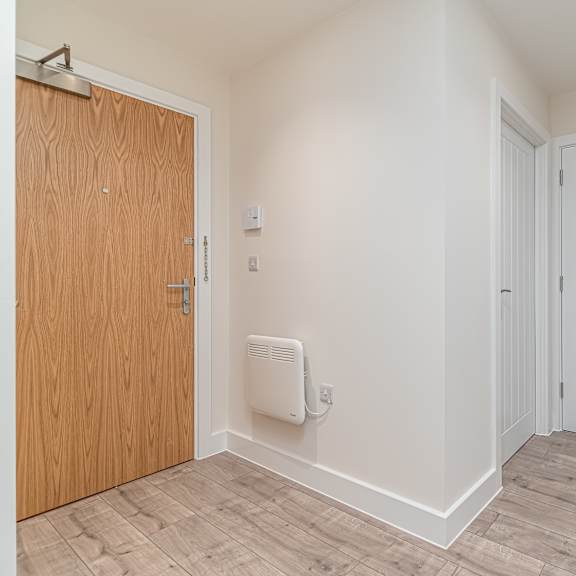 Thumbnail 9 of 12 A room with a wooden door and a white wall with a heater.