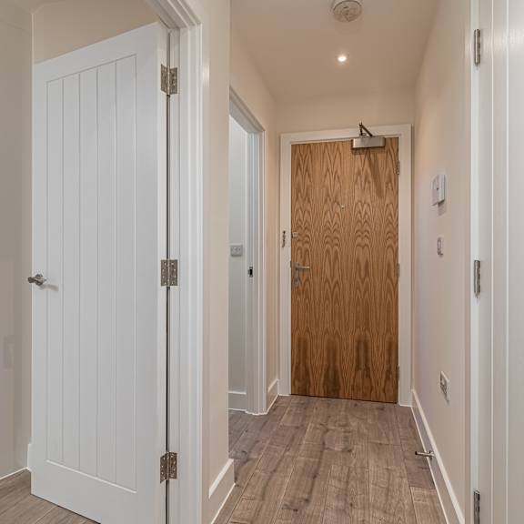 Thumbnail 7 of 9 A hallway with a white door on the left and a wooden door on the right.