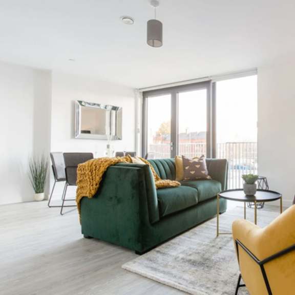 Thumbnail 5 of 8 a living room with a green couch and a large window at Vox Apartments, Manchester, M15 4YD