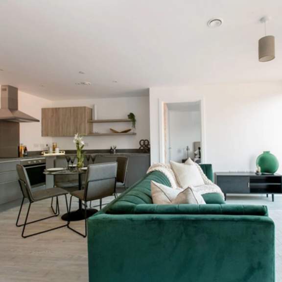 Thumbnail 5 of 7 a living room with a green couch and a kitchen with a table and chairs at Vox Apartments, Manchester