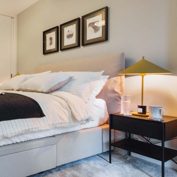 Thumbnail 1 of 5 A bedroom with a bed, a nightstand with a lamp, and a wardrobe.at Slate Yard Apartments, Salford