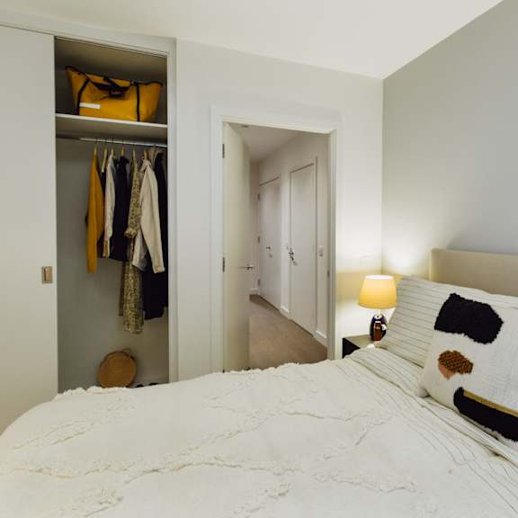 Thumbnail 4 of 8 A bedroom with a white bed and a closet with clothes hanging.at Slate Yard Apartments, Salford