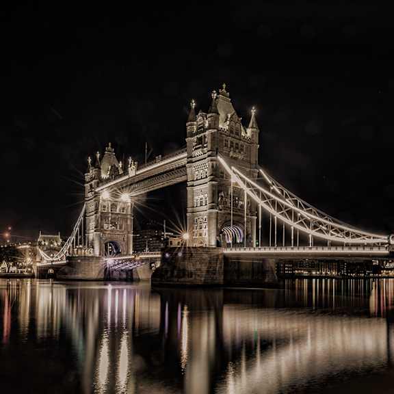 Thumbnail 2 of 3 A beautifully lit bridge at night with its reflection in the water.