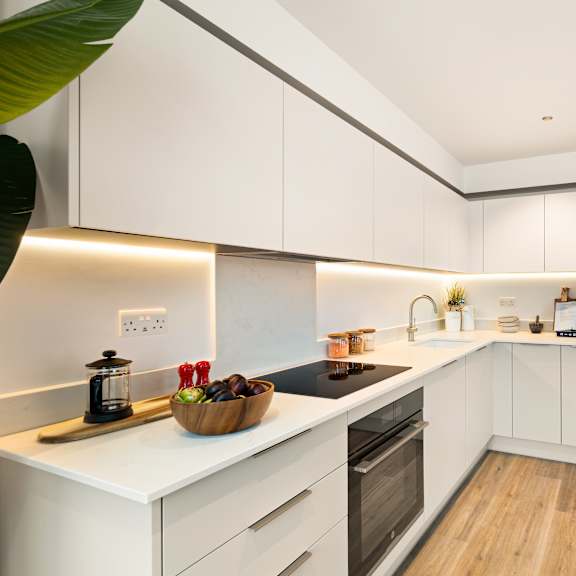 Thumbnail 2 of 4 A modern kitchen with white cabinets and a wooden floor.