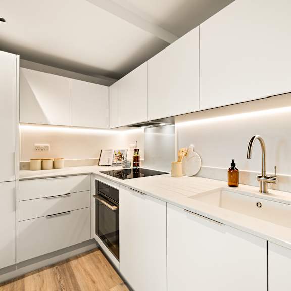 Thumbnail 1 of 4 A modern kitchen with white cabinets and a wooden floor.
