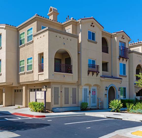A row of beige townhouses with green shutters and balconies.