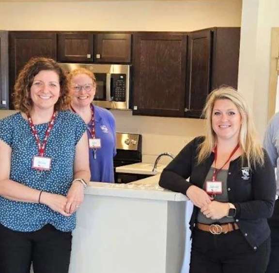 Two women wearing name tags stand in a kitchen.