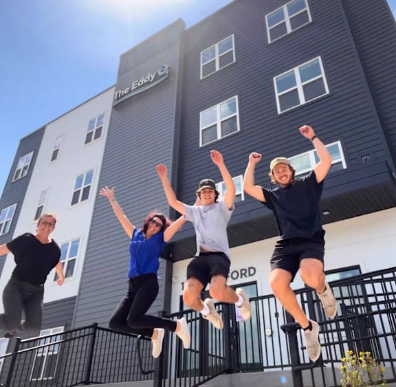 Four people jumping in front of a hotel.