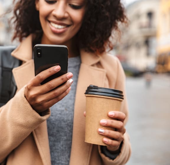 a woman in a camel coat holding a coffee cup and looking at her phone at Zeta Luxury Apartments in Sacramento, CA