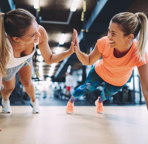 two girls high five each other while doing pushups in a gym