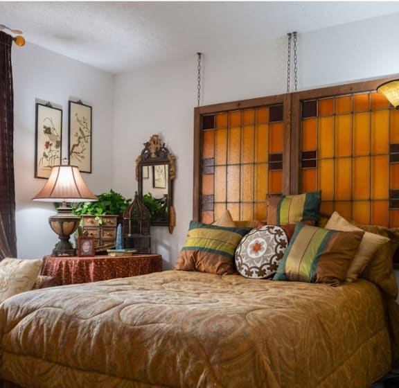 A bed with a yellow comforter and pillows sits in a room with a mirror and a plant.