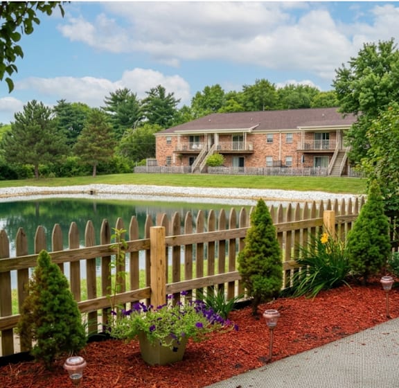 A wooden fence with a small garden in front of a brick building.